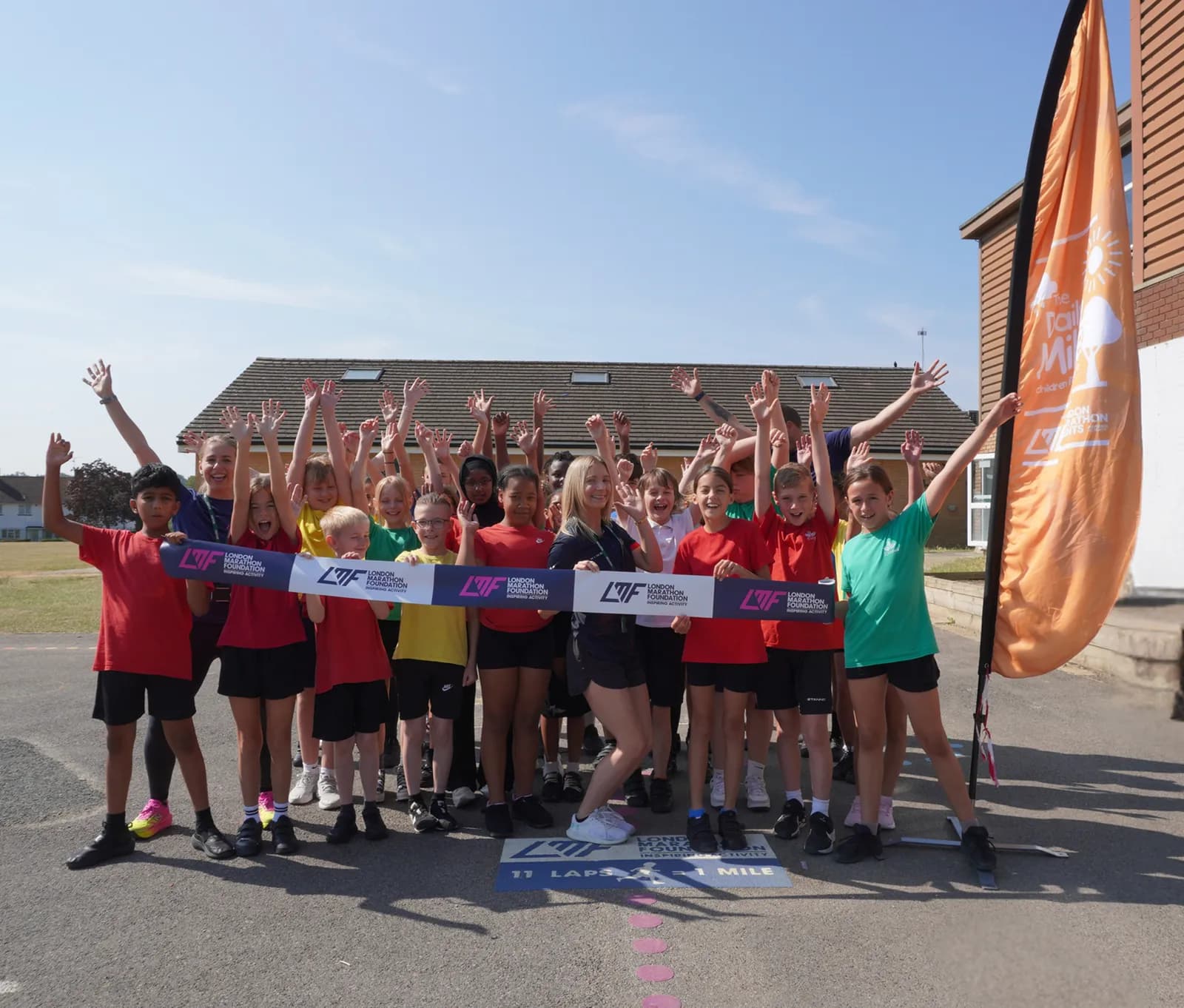 A group of cheerful children and adults with their hands raised, holding a banner for the London Marathon Foundation.